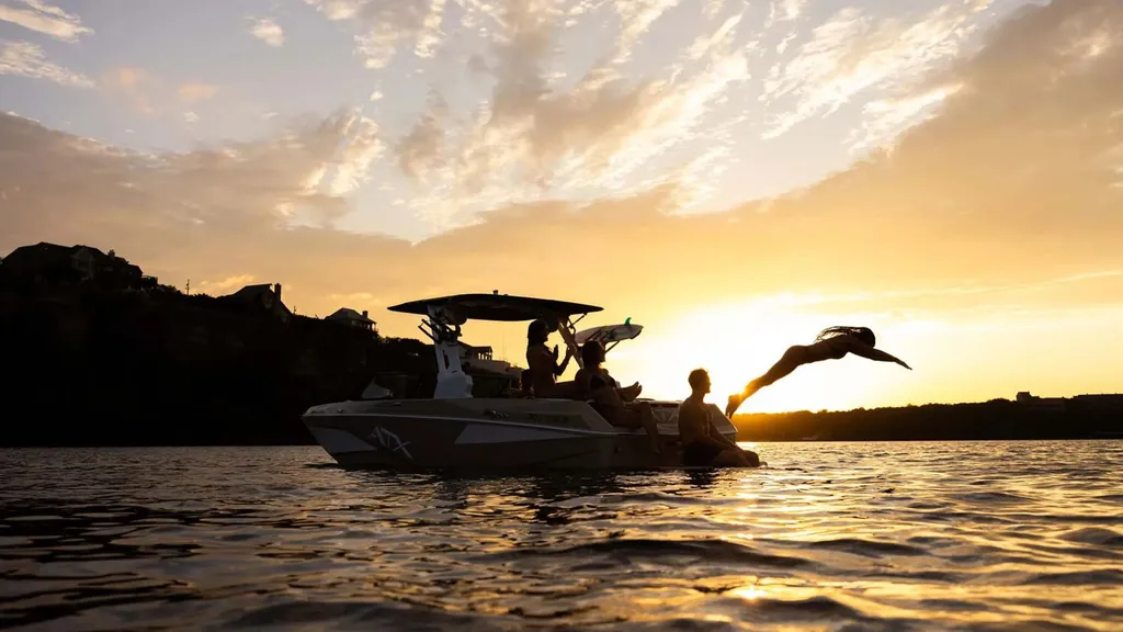 Family diving off a wake boat at sunset