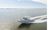 A white motorboat speeds across calm waters under a clear blue sky.