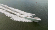 A white boat speeds across the water, leaving a wake behind it. The scene captures a dynamic view from above.